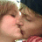 Two figures in close physical proximity with eyes closed, one figure's mouth near the other's cheek.