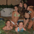 Group of people in swimwear gathered around a pool with a stone structure in the background.