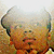 Pixelated static image of a person with light skin tone, brown hair styled in an updo, wearing orange clothing against a blurred background.