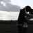 Pixelated image of a person in dark clothing holding another figure against a blurred outdoor background with text overlay.