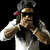 Pixelated figure in dark cap with red brim, white shirt, and dark vest, holding hands near face against black background.