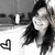 A grayscale image of a person with long dark hair smiling, wearing a white top and hat, with a heart symbol in the lower-left corner.