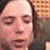 A pixelated close-up of a person's face with closed eyes, light skin tone, and dark hair against a blurred background with brown and beige tones.
