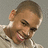 Pixelated close-up of a person with short brown hair, closed eyes, and a wide open mouth showing teeth and tongue, wearing a light-colored shirt against a gray background.