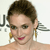 A pixelated close-up of a person with short brown hair, wearing gold earrings and red lipstick, against a light background with partial dark text.