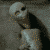 A skeletal figure with a blank expression sits in a dark, textured background, its head and arms shifting slightly across frames.