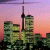 Pixelated static image of a cityscape at sunset featuring tall buildings and a prominent tower against a gradient sky.