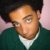 Pixelated close-up of a person with light skin, dark hair, and green clothing against pink background.