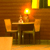 Pixelated scene of a wooden table with two chairs, a lamp, and a bottle under warm lighting.