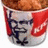 A KFC bucket with Colonel Sanders' face on it, filled with fried chicken, against a red background with blue pixelated text.