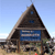 Pixelated image of a triangular wooden structure with a blue signboard, set against a clear sky background.