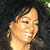 Pixelated close-up of a person's face with light skin tone, dark hair, and a smiling expression against a dark background.