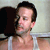Static 50x50 pixel AIM buddy icon showing a close-up of a person's face and upper torso with dark hair, light skin tone, and visible facial features including eyes, nose, mouth, and ear, wearing a white tank top against a blurred background.