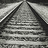 Black-and-white pixelated image of railroad tracks extending into the distance with overlaid text reading "Love Is A Long Road Down The Path To Heartache" in a retro digital font.