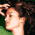 Static pixelated image of a person's profile with dark curly hair, light skin tone, and visible ear stud against green background.