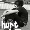 Black-and-white image of a person crouching with arms crossed, wearing dark clothing and patterned shorts, with large white text reading 'hurt' overlaid at the bottom.