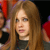 A pixelated close-up of a person with long light brown hair wearing a dark top, with partial red and purple elements in the background.