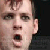 Pixelated close-up of a person's face with mouth open, dark background, and visible ear.