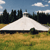 A pixelated landscape image shows a large white tent-like structure on a grassy field with trees and blue sky in the background.