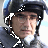 Pixelated image of a person wearing a dark helmet with white checkered patterns and a dark jacket with white accents, set against a light background.