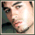 Pixelated close-up of a person's face with light skin tone, dark eyebrows, and dark eyes, framed by a thin border.