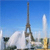 Pixelated static image of a tall dark tower with a lattice structure against a blue sky, with white clouds and a shorter white tower nearby.