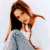 Pixelated image of a person with long brown hair wearing dark top and light blue pants, head tilted left against soft pastel background.