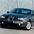 A blue sedan with silver accents is positioned at a slight angle on a light gray surface, viewed from the front-left side with a blurred background.
