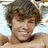 Pixelated close-up of a person with curly brown hair, light skin tone, and visible facial features including eyes, nose, mouth, and chin.