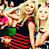 Two blonde women pose in front of a blurred crowd; one wears a black dress with red stripes, the other a blue and white outfit with a black wristband.