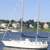 Pixelated static image of a white sailboat on blue water with green shoreline and trees under a light blue sky.