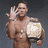 A shirtless man with a muscular build holds a large rectangular trophy, waves his right hand, and wears two necklaces against a dark gray background.