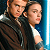 Pixelated static image of two human figures in close proximity, one holding a glowing blue lightsaber-like object against a dark background with blue vertical elements.