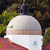 A pixelated static image shows a white domed building with a small green patch on its upper left side, set against a blurred background of green and brown foliage.