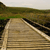 A static pixelated image shows a light brown wooden structure with horizontal planks and a diagonal white stripe, set against a blurred green and brown background.