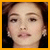 Pixelated close-up of a person's face with brown hair, wearing earrings and dark clothing against a black background.