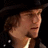 Pixelated profile view of a person with brown hair wearing a dark hat and light-colored shirt against a black background.