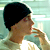 Static pixelated image of a person in profile with dark hair and light skin, holding an object near their mouth against a gradient background.