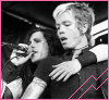 Black-and-white photo of two people in a vehicle, one holding a microphone; pink text overlays change across frames.