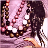 A person with long dark hair wears multiple beaded necklaces in pink, white, brown, and black against a light purple fabric background.