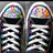 Black sneakers with white laces and multicolored accents on the toe caps, paired with gray shorts featuring a heart symbol.