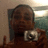 Pixelated image of a person with dark hair and a light-colored shirt holding a small object against a blurred background.
