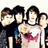 Group of seven people in dark clothing with one person wearing a white shirt featuring red and blue graphic design, standing closely together against light background.