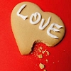 A heart-shaped cookie with a bite taken out, decorated with white icing spelling 'LOVE' on a solid red background.