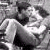 Black-and-white pixelated image of a person lying down with arms crossed, next to text reading "Never Leave Me" on gray background.