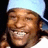A person wearing a light blue headwrap and white shirt smiles broadly across three showing slight facial movement