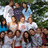 A pixelated group photo of people in front of greenery with bright cyan background and red pixelated text.