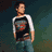 A pixelated figure in a white and black long-sleeve shirt with red accents, blue jeans, and hands in pockets against a dark green background.