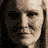 A static icon featuring a woman's face, yellow chevron arrows, and text reading "THE WARDEN" and "DEATH RACE" on a black background.