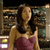 A pixelated image of a person with long brown hair wearing a sleeveless maroon top, standing in front of a blurred background with indistinct shapes and colors.